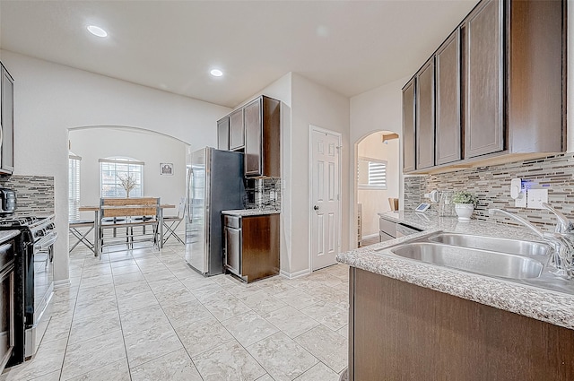 kitchen with sink, tasteful backsplash, gas stove, dark brown cabinetry, and stainless steel refrigerator