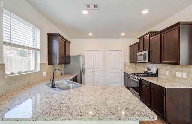 kitchen featuring appliances with stainless steel finishes, backsplash, light stone counters, dark brown cabinetry, and sink