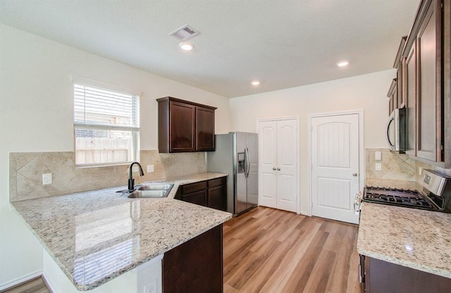 kitchen featuring sink, light hardwood / wood-style flooring, light stone countertops, appliances with stainless steel finishes, and kitchen peninsula