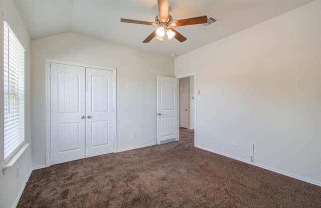 unfurnished bedroom with ceiling fan, a closet, lofted ceiling, and dark colored carpet