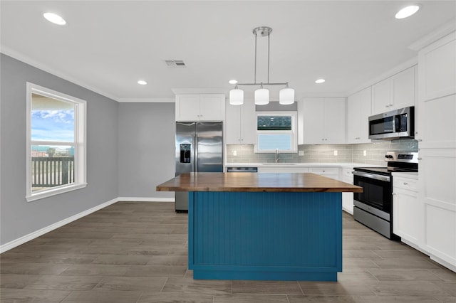 kitchen with wood counters, appliances with stainless steel finishes, sink, pendant lighting, and a center island