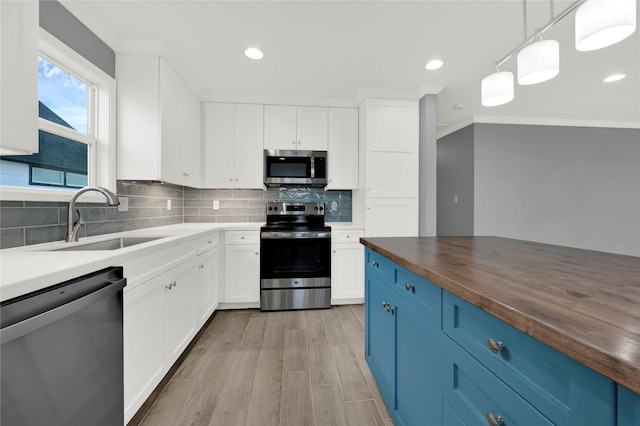 kitchen with blue cabinetry, hanging light fixtures, wood counters, white cabinets, and appliances with stainless steel finishes