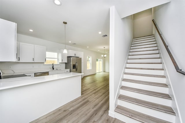 kitchen with sink, hanging light fixtures, stainless steel appliances, light hardwood / wood-style floors, and white cabinets