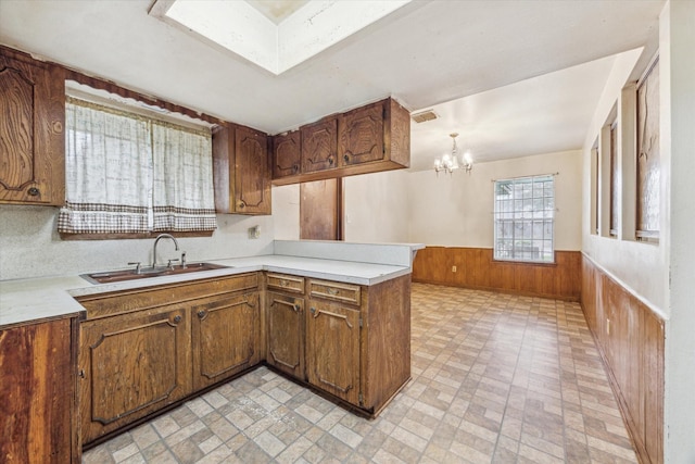 kitchen with kitchen peninsula, sink, pendant lighting, a chandelier, and wood walls