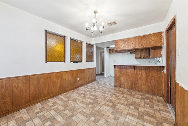 kitchen featuring kitchen peninsula, pendant lighting, wooden walls, and a notable chandelier