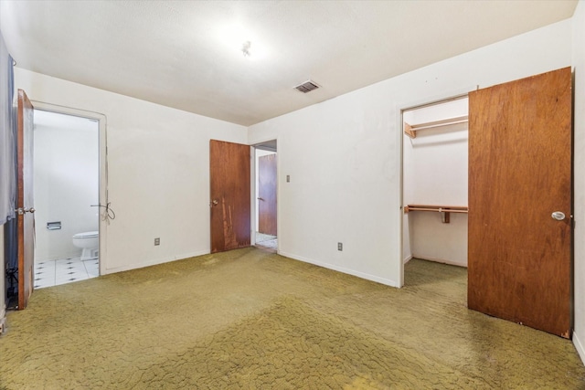 unfurnished bedroom featuring a walk in closet, a closet, carpet floors, and ensuite bath