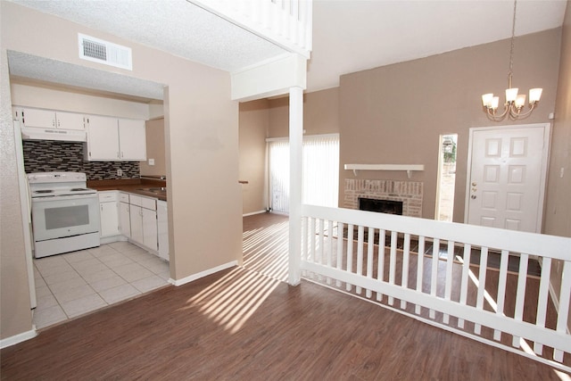 kitchen featuring backsplash, a brick fireplace, white range with electric stovetop, decorative light fixtures, and white cabinets