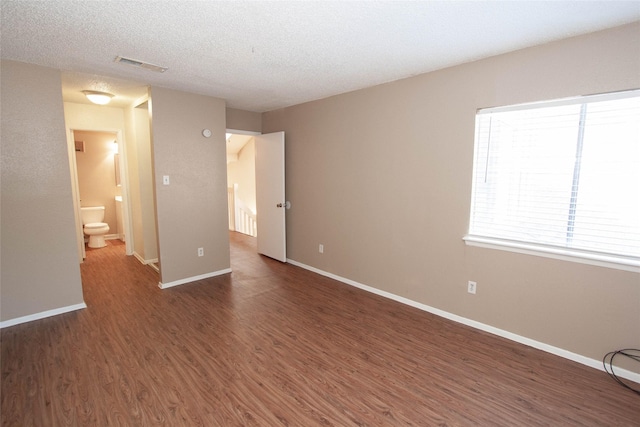 unfurnished bedroom with a textured ceiling, ensuite bathroom, and dark hardwood / wood-style floors