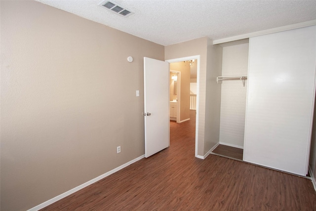 unfurnished bedroom featuring dark hardwood / wood-style flooring, a textured ceiling, and a closet