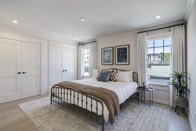 bedroom with two closets, crown molding, and light hardwood / wood-style floors