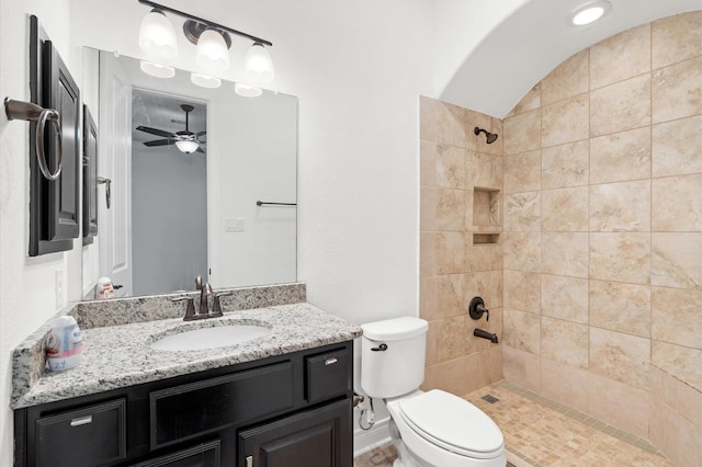 bathroom with a tile shower, vanity, toilet, and ceiling fan