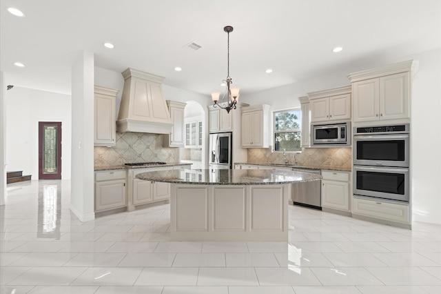 kitchen featuring appliances with stainless steel finishes, custom exhaust hood, pendant lighting, dark stone countertops, and a center island