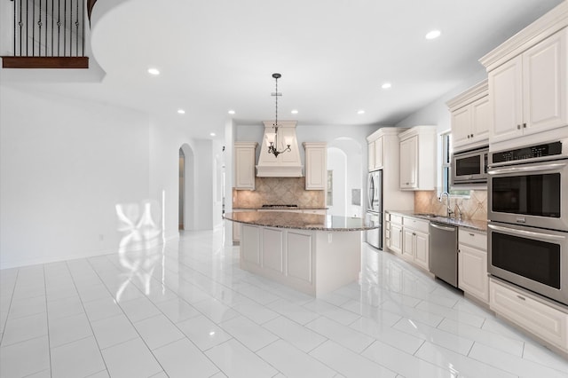 kitchen with light stone countertops, a center island, hanging light fixtures, decorative backsplash, and appliances with stainless steel finishes