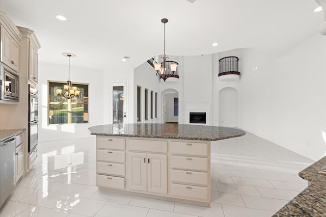 kitchen featuring appliances with stainless steel finishes, a notable chandelier, dark stone countertops, a kitchen island, and hanging light fixtures