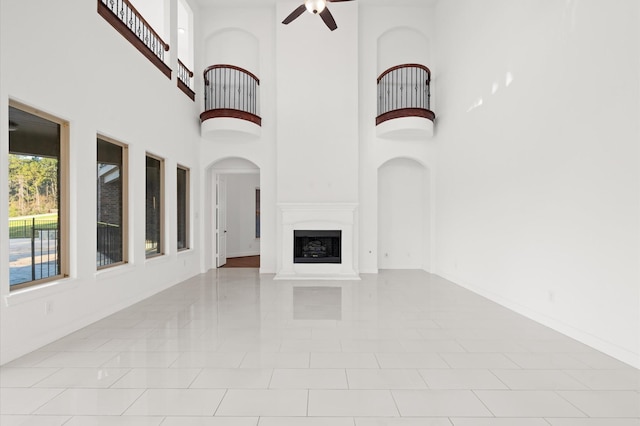 unfurnished living room with ceiling fan, light tile patterned flooring, and a high ceiling