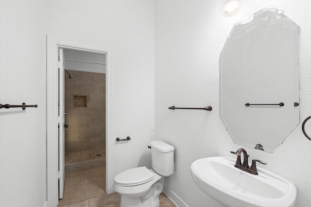 bathroom featuring tile patterned flooring, tiled shower, toilet, and sink