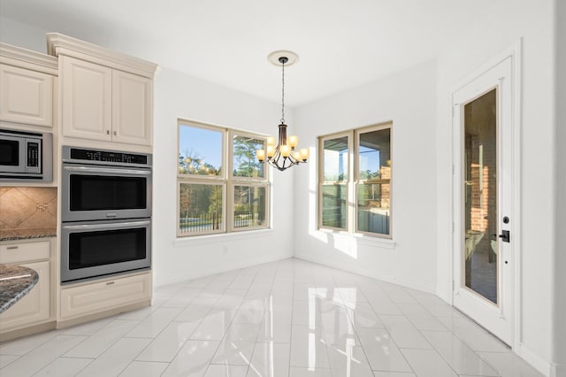 kitchen with dark stone counters, cream cabinets, light tile patterned flooring, stainless steel appliances, and a chandelier