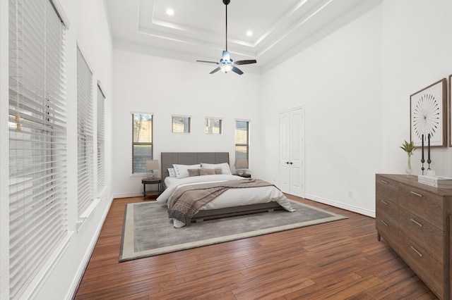 bedroom featuring a tray ceiling, ceiling fan, dark hardwood / wood-style flooring, and a towering ceiling