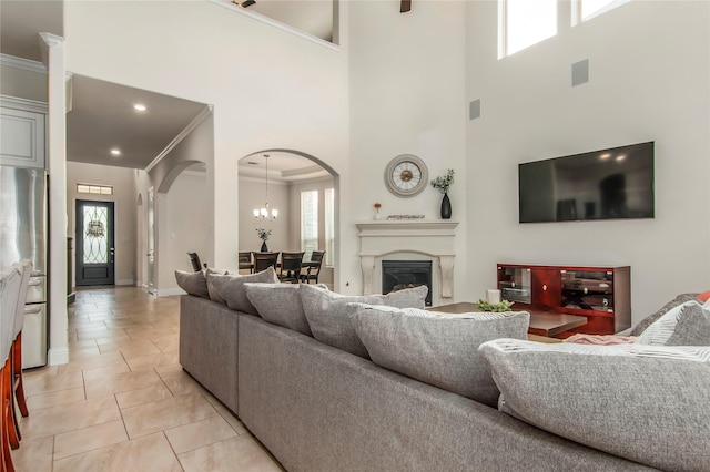 living room featuring light tile patterned floors, ornamental molding, a towering ceiling, and a chandelier