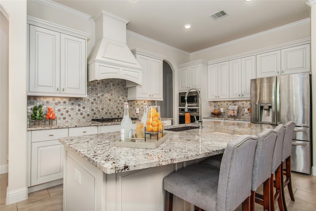 kitchen featuring decorative backsplash, stainless steel appliances, premium range hood, and a kitchen island with sink