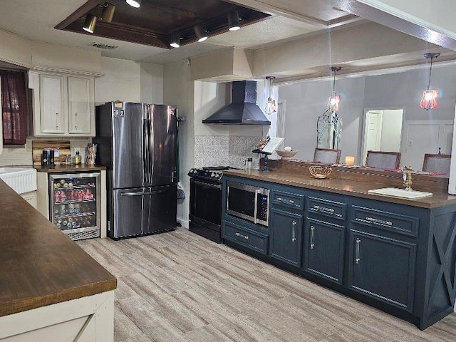 kitchen with appliances with stainless steel finishes, beverage cooler, wall chimney range hood, white cabinetry, and hanging light fixtures