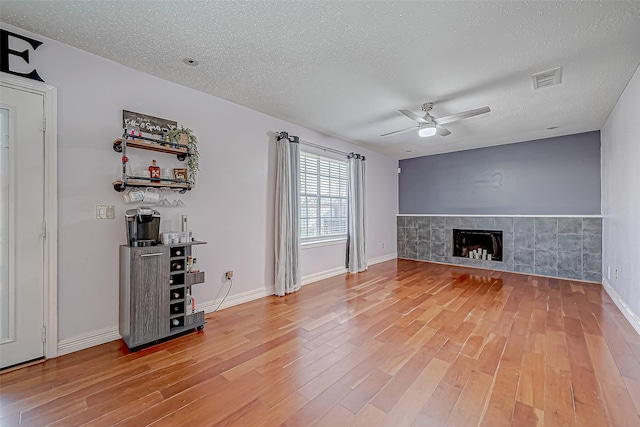 unfurnished living room featuring hardwood / wood-style floors, a textured ceiling, ceiling fan, and a tiled fireplace