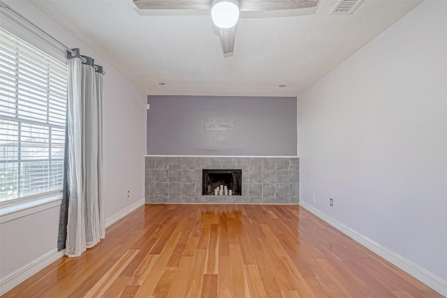 unfurnished living room featuring wood-type flooring, a textured ceiling, ceiling fan, and a tiled fireplace