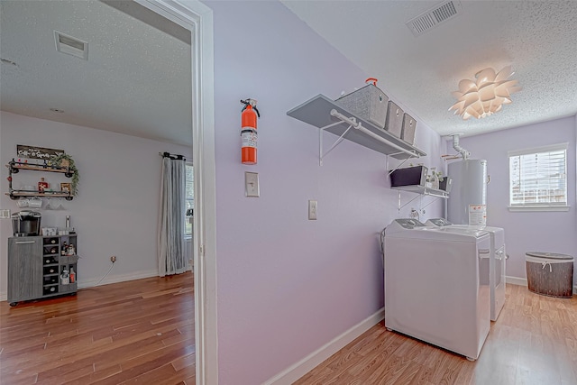 clothes washing area with water heater, washer and clothes dryer, light hardwood / wood-style floors, and a textured ceiling