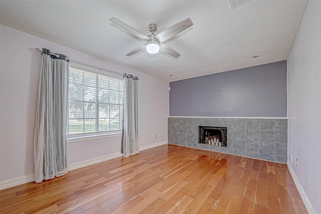 unfurnished living room with a tile fireplace, hardwood / wood-style floors, a textured ceiling, and ceiling fan