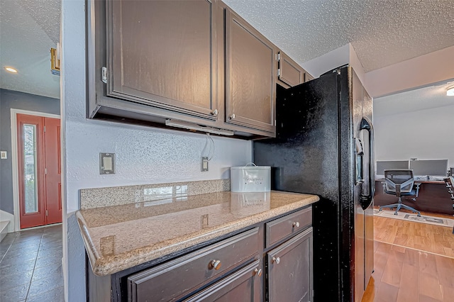 kitchen with black fridge with ice dispenser, light stone countertops, a textured ceiling, and light hardwood / wood-style flooring