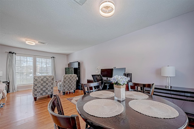 dining room featuring light wood-type flooring and a textured ceiling