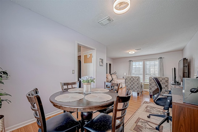 dining space with a textured ceiling and light hardwood / wood-style flooring