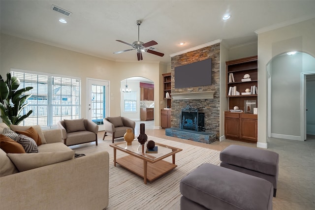 living room with a stone fireplace, light tile patterned flooring, ceiling fan with notable chandelier, and ornamental molding