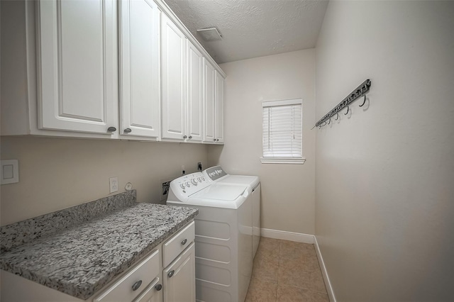 clothes washing area featuring washer and dryer, light tile patterned flooring, cabinets, and a textured ceiling