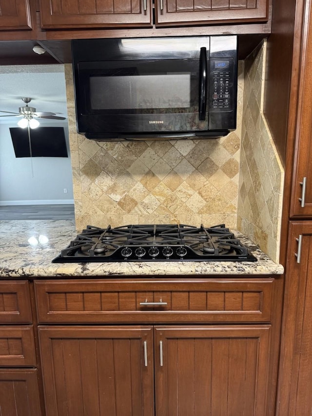 kitchen with black appliances, ceiling fan, light stone counters, and tasteful backsplash