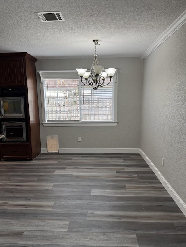 unfurnished dining area with a chandelier, a textured ceiling, dark hardwood / wood-style flooring, and ornamental molding