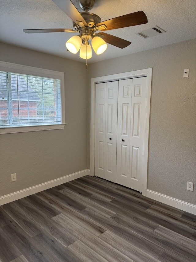 unfurnished bedroom with a textured ceiling, dark hardwood / wood-style flooring, a closet, and ceiling fan