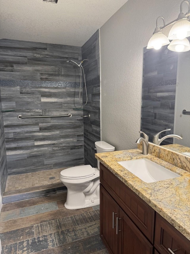 bathroom featuring vanity, toilet, a textured ceiling, and a tile shower