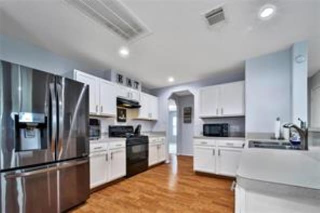 kitchen featuring white cabinets, black appliances, extractor fan, and light wood-type flooring