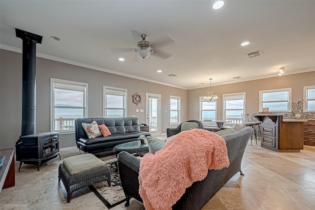 living room featuring ceiling fan with notable chandelier, a wood stove, crown molding, and a wealth of natural light