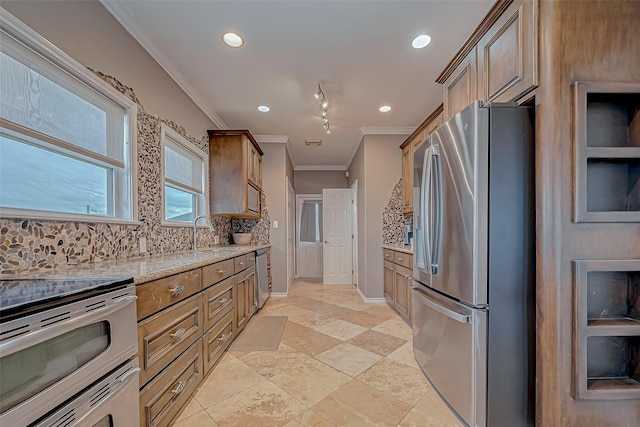 kitchen with tasteful backsplash, light stone counters, stainless steel appliances, crown molding, and sink