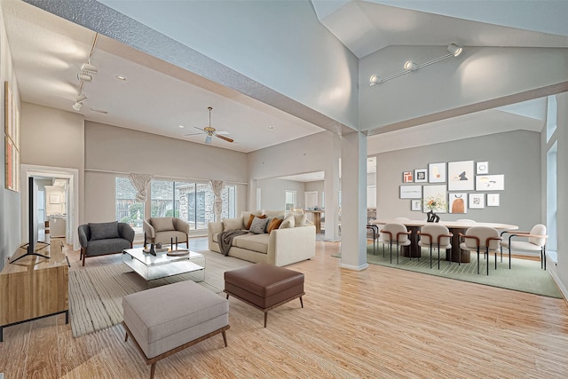 living room with ceiling fan, light hardwood / wood-style flooring, track lighting, and a high ceiling