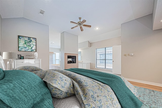 bedroom with hardwood / wood-style flooring, ceiling fan, a tiled fireplace, and vaulted ceiling