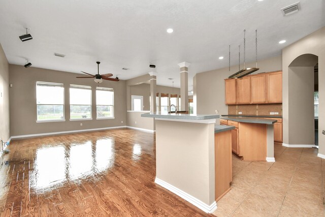 kitchen with ceiling fan, sink, backsplash, a kitchen island with sink, and light brown cabinetry