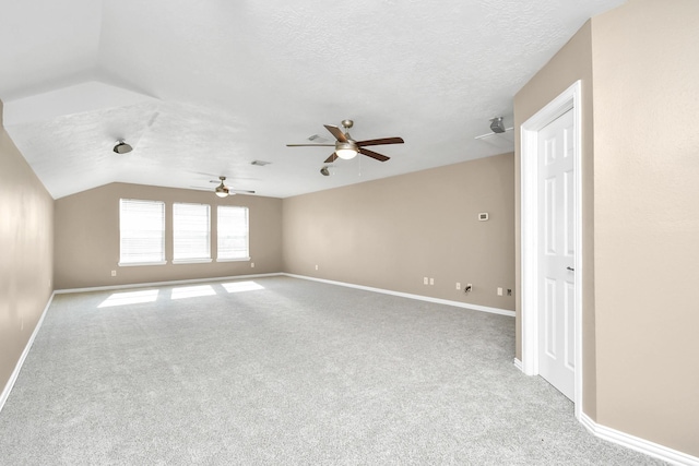 empty room featuring a textured ceiling, light colored carpet, vaulted ceiling, and ceiling fan