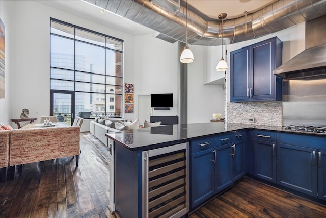 kitchen featuring stainless steel gas stovetop, wall chimney range hood, blue cabinetry, and beverage cooler