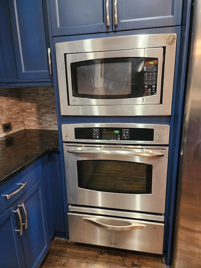 kitchen featuring dark stone counters, blue cabinets, dark hardwood / wood-style floors, tasteful backsplash, and stainless steel appliances