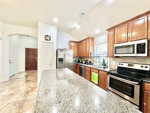 kitchen featuring light stone countertops, appliances with stainless steel finishes, backsplash, vaulted ceiling, and sink