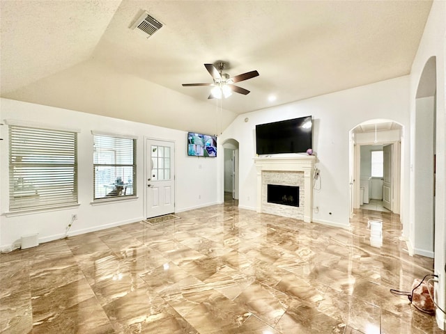 unfurnished living room with ceiling fan, a stone fireplace, lofted ceiling, and a textured ceiling