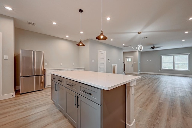 kitchen featuring ceiling fan, a center island, hanging light fixtures, and stainless steel refrigerator